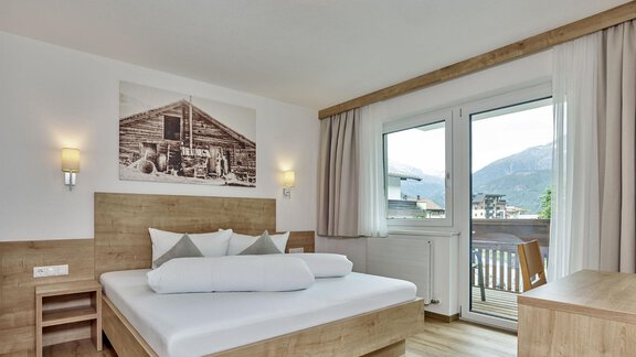 Ein modernes Zimmer mit einem Holzbetten und einem Balkon. Große Fenster bieten einen Blick auf die Berge und viel Tageslicht. - Gästehaus Bergkristall - Sölden