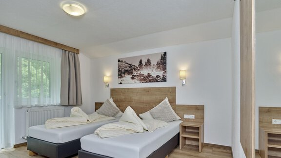 A modern bedroom with two single beds and wooden decor. The walls are bright, and a large window provides plenty of daylight. - Gästehaus Bergkristall - Sölden