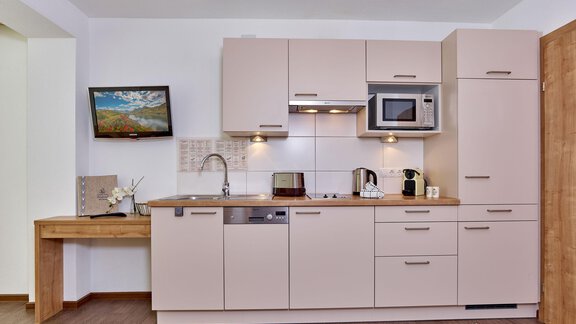 Eine moderne Küche mit hellen Schränken und einem Holzarbeitsplatz. Im Hintergrund hängt ein Gemälde an der Wand. - Gästehaus Bergkristall - Sölden
