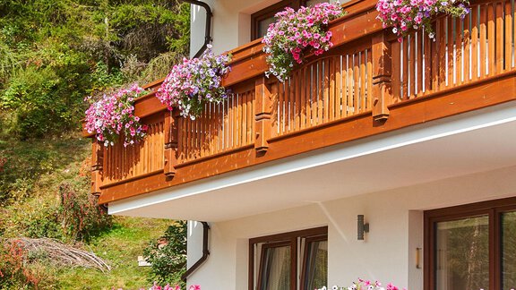 Ein charmanter Holzbau mit Balkonen, die mit bunten Blumen geschmückt sind. Im Hintergrund ist eine grüne, bewaldete Landschaft zu sehen. - Gästehaus Bergkristall - Sölden