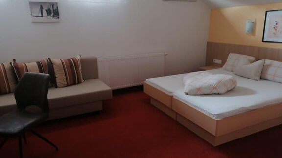 Ein gemütliches Zimmer mit einem Doppelbett und einer Couch. Die Wände sind hell, und der Boden ist mit Teppich ausgelegt. - Gästehaus Sternberger - Sölden