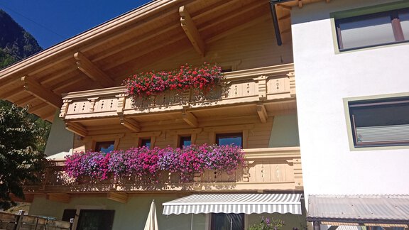 Ein schönes Holzhaus mit blühenden Balkonkästen. Die Fassade ist hell, und der Himmel ist blau. - Gästehaus Sternberger - Sölden
