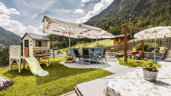 Ein schöner Garten mit einem Spielplatz und einem Esstisch unter Sonnenschirmen. Die umliegenden Berge und die gute Wetterlage schaffen eine einladende Atmosphäre. - Gasthof Granstein - Sölden