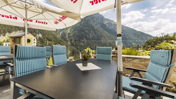 Eine gemütliche Terrasse mit modernen Stühlen und einem Tisch. Im Hintergrund sind majestätische Berge und ein blauer Himmel zu sehen. - Gasthof Granstein - Sölden