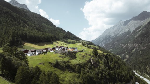 Ein malerisches Tal mit grünen Wiesen und einem kleinen Dorf zwischen den Bergen. Die Wolken ziehen am Himmel vorbei und die Natur ist üppig und einladend. - Gasthof Granstein - Sölden