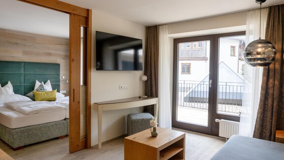 A modern hotel room with a double bed, television, and a desk. Large windows let in plenty of daylight and provide a view outside. - Glanz & Glory Hotel - Sölden
