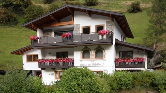A beautiful house with balconies, decorated with blooming plants. It is located surrounded by a green landscape. - Haus am Wildbach - Sölden