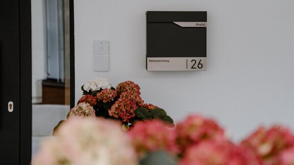 Ein Briefkasten mit der Nummer 126 an einer Wand. Im Vordergrund sind bunte Blumen zu sehen. - Haus Crystal - Sölden