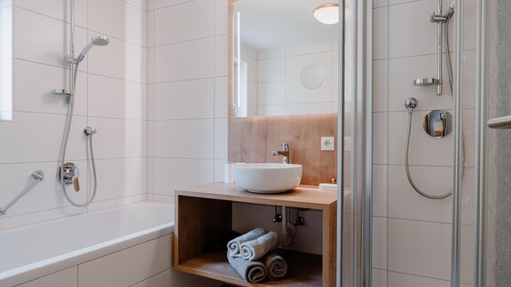 Ein modernes Badezimmer mit einer Badewanne und einer Dusche. Auf einem Holzregal liegen mehrere Handtücher bereit. - Haus Crystal - Sölden