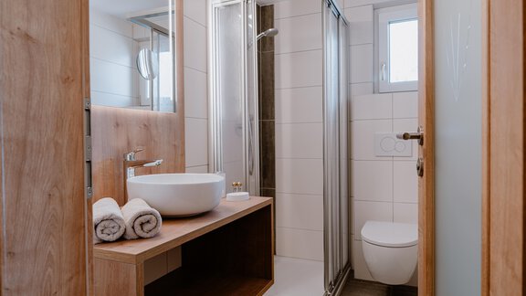 Ein modernes Badezimmer mit einer Dusche und einem Waschbecken. Es ist hell und minimalistisch gestaltet, mit Holz- und Flieselementen. - Haus Crystal - Sölden