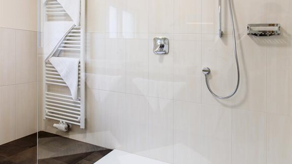 A modern shower with a glass partition in a bright bathroom. The floor is tiled with dark tiles, and a towel holder is mounted on the wall. - Haus Madeleine - Sölden