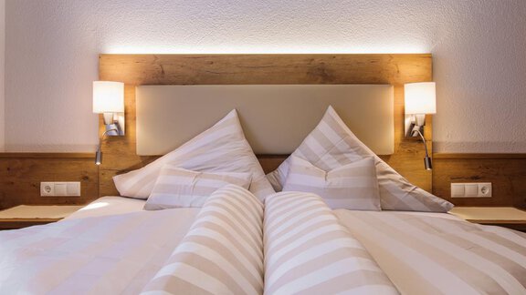 A cozy bedroom with a double bed and padded headboard. The soft lighting and striped bed covers create a relaxed atmosphere. - Haus Madeleine - Sölden