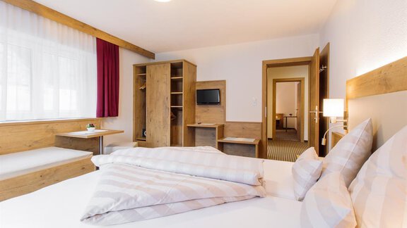 A cozy bedroom with wooden decor and plenty of light. The room features a large bed, a small desk, and a wardrobe. - Haus Madeleine - Sölden