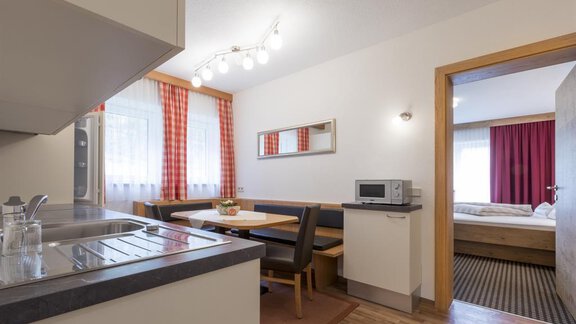 Eine moderne Küche mit einem Esstisch und Stühlen. Im Hintergrund ist ein Schlafzimmer sichtbar. - Haus Madeleine - Sölden