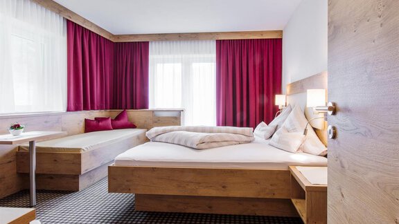 Ein modernes Schlafzimmer mit Holzmöbeln und roten Vorhängen. Es gibt ein Doppelbett und ein zusätzliches Bett sowie einen Tisch. - Haus Madeleine - Sölden