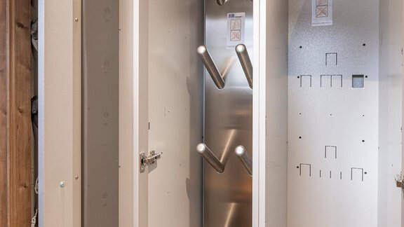 Ein moderner, schmaler Schrank mit einer Metallaufhängung für Kleidungsstücke. Die Innenseite ist schlicht und hell gestaltet. - Haus Manfred - Sölden