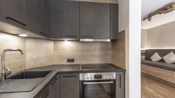 Moderne Küche mit dunklen Schränken und Edelstahlgeräten. Der Raum hat eine helle, warme Atmosphäre. - Haus Manfred - Sölden