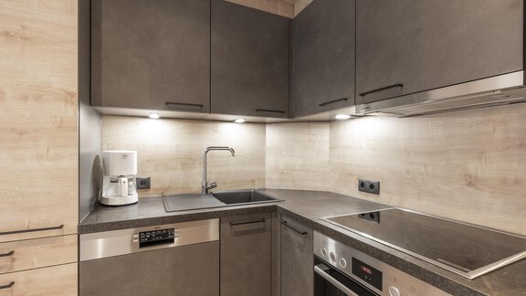 Eine moderne Küche mit dunklen Schränken und einer funktionalen Anordnung. Der Raum ist gut beleuchtet und enthält Geräte wie einen Wasserkocher und einen Herd. - Haus Manfred - Sölden