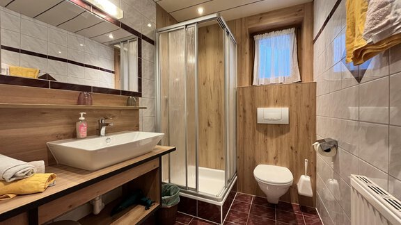 Ein modernes Badezimmer mit einer Dusche, einem Waschbecken und einem WC. Die Wände sind teilweise mit Holz und Fliesen verkleidet, und es gibt Handtücher in warmen Farben. - Haus Moosbichl - Sölden