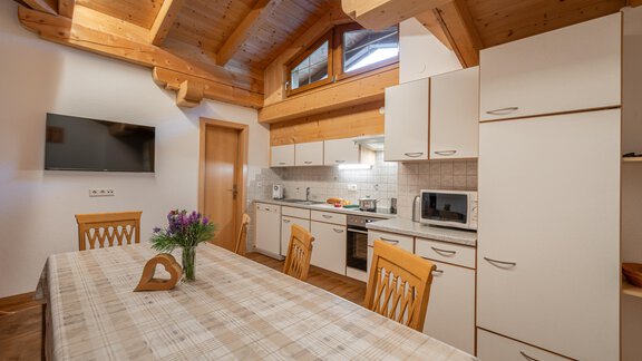 A cozy fully equipped kitchen with a wooden ceiling and a large dining table. - Haus Nicola - Sölden