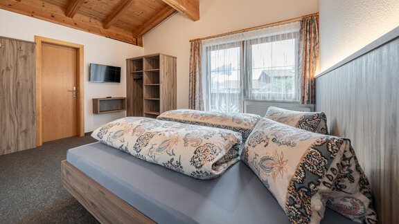 A cozy bedroom with a double bed and decorative pillows. The room features wooden ceilings and windows with curtains that let in plenty of light. - Haus Nicola - Sölden