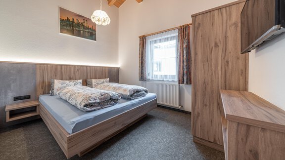 A modern bedroom with a double bed and wooden surfaces. The room has large windows and a warm, inviting atmosphere. - Haus Nicola - Sölden