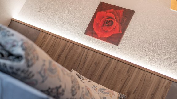 A cozy room with a soft pillow and a wall painting of a red rose. The lighting creates a warm atmosphere. - Haus Nicola - Sölden