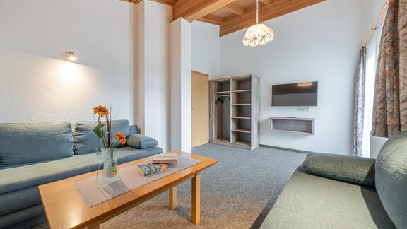 A bright living room with two sofas and a wooden table. On the wall, there is a television and storage shelves. - Haus Nicola - Sölden