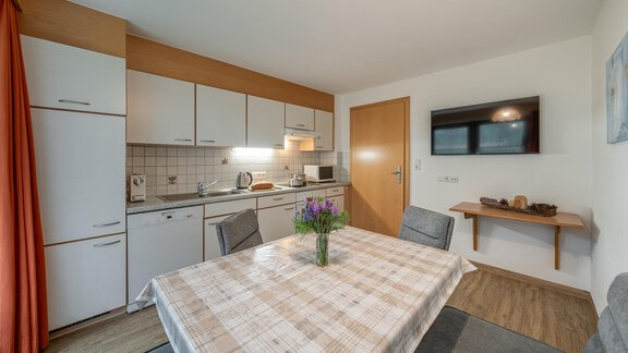 A modern kitchen with a dining table and four chairs. The walls are bright, and there is a large window front with curtains. - Haus Nicola - Sölden