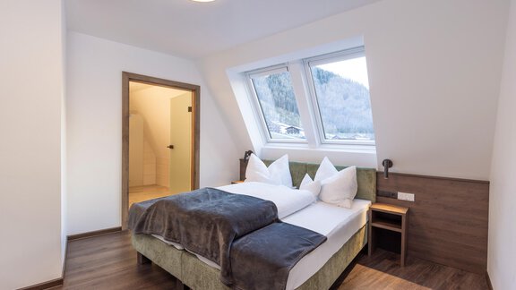 Ein modernes Schlafzimmer mit einem komfortablen Bett und großen Fenstern. Der Raum ist hell und einladend, mit einem Holzfußboden und schlichten Möbeln. - Home4You - Sölden