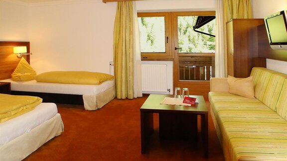 Ein gemütliches Hotelzimmer mit zwei Betten und einer Couch. Große Fenster bieten Ausblick und Tageslicht. - Hotel Garni Hainbacherhof - Sölden