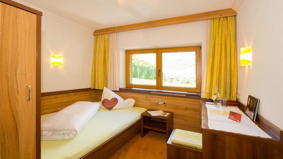 Ein gemütliches Schlafzimmer mit einem Einzelbett und Holzmöbeln. Große Fenster lassen viel Licht herein und bieten einen Blick auf die Umgebung. - Hotel Garni Hainbacherhof - Sölden