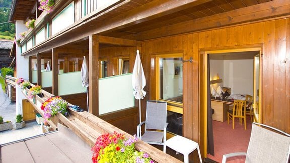 Ein gemütlicher Balkon mit Blumen und Stühlen, der Blick auf ein Holzgebäude. Im Hintergrund sieht man ein helles Zimmer mit einem Tisch und Stühlen. - Hotel Garni Hainbacherhof - Sölden