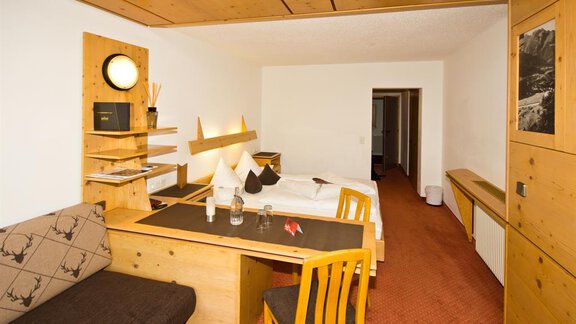Ein gemütliches Zimmer mit Holzdekor und einem Einzelbett. Ein Tisch mit Stühlen und einem Sofa schaffen eine einladende Atmosphäre. - Hotel Garni Hainbacherhof - Sölden