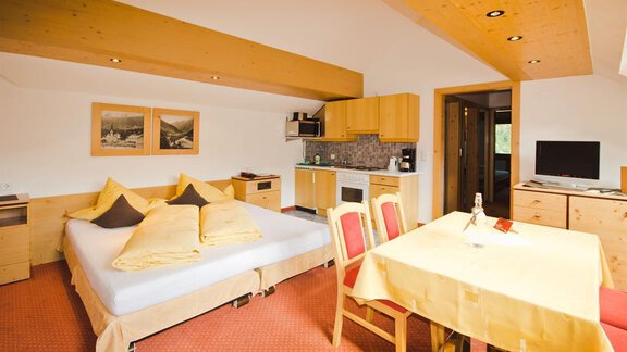Ein gemütliches Zimmer mit einem Doppelbett, einer kleinen Küchenzeile und einem Essbereich. Die Holzelemente und die warmen Farben schaffen eine einladende Atmosphäre. - Hotel Garni Hainbacherhof - Sölden