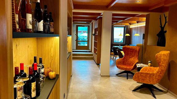 Ein modern gestalteter Empfangsbereich mit Holzregalen und gemütlichen orangen Sessel. Auf einem Regal sind mehrere Flaschen Wein und ein kurzer Tisch dekoriert. - Hotel Garni Hainbacherhof - Sölden