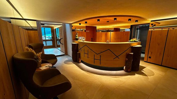 Ein modernes Empfangsbereich mit einer runden Theke aus Holz. Gemütliche Sitzgelegenheiten und indirektes Licht sorgen für eine einladende Atmosphäre. - Hotel Garni Hainbacherhof - Sölden