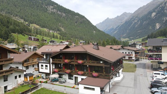 Eine malerische alpine Landschaft mit einem charmanten Hotel und grünen Wiesen. Im Hintergrund sind majestätische Berge zu sehen. - Hotel Garni Maria Theresia - Sölden