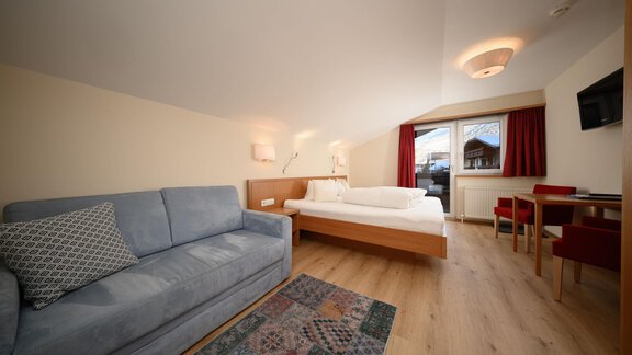 Ein modernes Zimmer mit einem bequemen Sofa und einem Doppelbett. Es gibt einen Tisch mit Stühlen und ein Fenster, das viel Tageslicht hereinlässt. - Hotel Garni Maria Theresia - Sölden