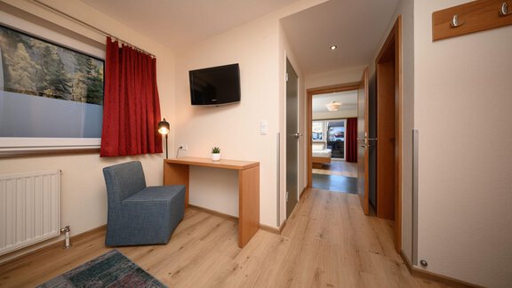 Ein gemütlicher Raum mit einem blauen Stuhl, einem Tisch und einem Fernseher an der Wand. Im Hintergrund sind Türen zu anderen Räumen sichtbar. - Hotel Garni Maria Theresia - Sölden