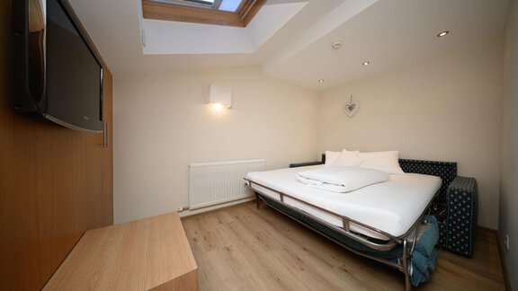 Ein modernes Zimmer mit einem Bett und einem Fernseher. Das Dachfenster sorgt für viel Tageslicht. - Hotel Garni Maria Theresia - Sölden