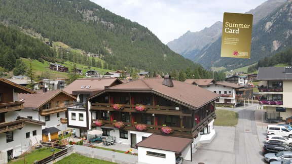 Ein alpenländliches Gebäude mit Balkonen und bunten Blumen. Im Hintergrund sind grüne Berge und eine ruhige Landschaft zu sehen. - Hotel Garni Maria Theresia - Sölden