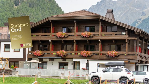 Ein gemütliches Hotel mit Holzbalkonen und blühenden Pflanzen. Im Vordergrund steht ein Auto und im Hintergrund sind Berge zu sehen. - Hotel Garni Maria Theresia - Sölden