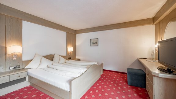 Ein helles Hotelzimmer mit zwei Einzelbetten und einem gemütlichen Teppichboden. Neben dem Bett steht ein Fernseher und ein kleiner Tisch. - Hotel Sölderhof - Sölden