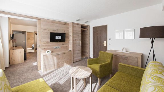 A modern room with wooden furniture and a cozy seating area. There is a TV and plenty of daylight. - Hotel Tyrolerhof - Sölden