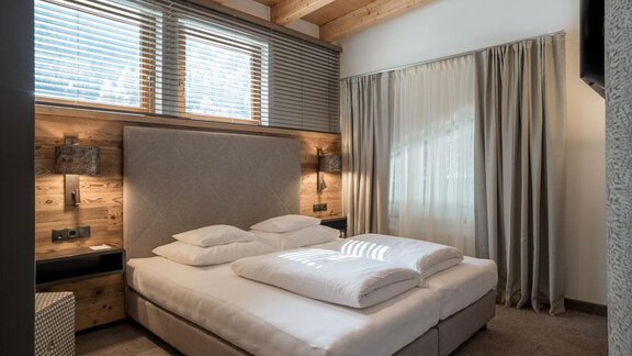 A modern bedroom with a large double bed and wooden details. The windows let in plenty of daylight and create a cozy atmosphere. - Hotel Tyrolerhof - Sölden