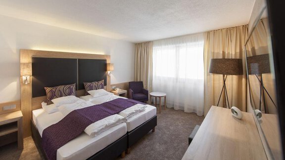 A modern hotel room with a double bed and elegant furnishings. Large windows let in plenty of daylight. - Hotel Tyrolerhof - Sölden