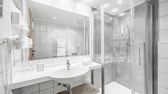 A modern bathroom with a shower and a sink. The walls are light-tiled and there are features such as a hairdryer. - Hotel Tyrolerhof - Sölden