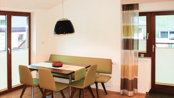 A modern dining area with a table and green chairs. The room has large windows and soft lighting conditions. - Lutonia Appartements Sölden - Sölden