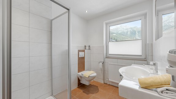 A modern bathroom with a shower and a sink. Bright tiles and plenty of daylight create a pleasant atmosphere. - Pension Charly - Sölden